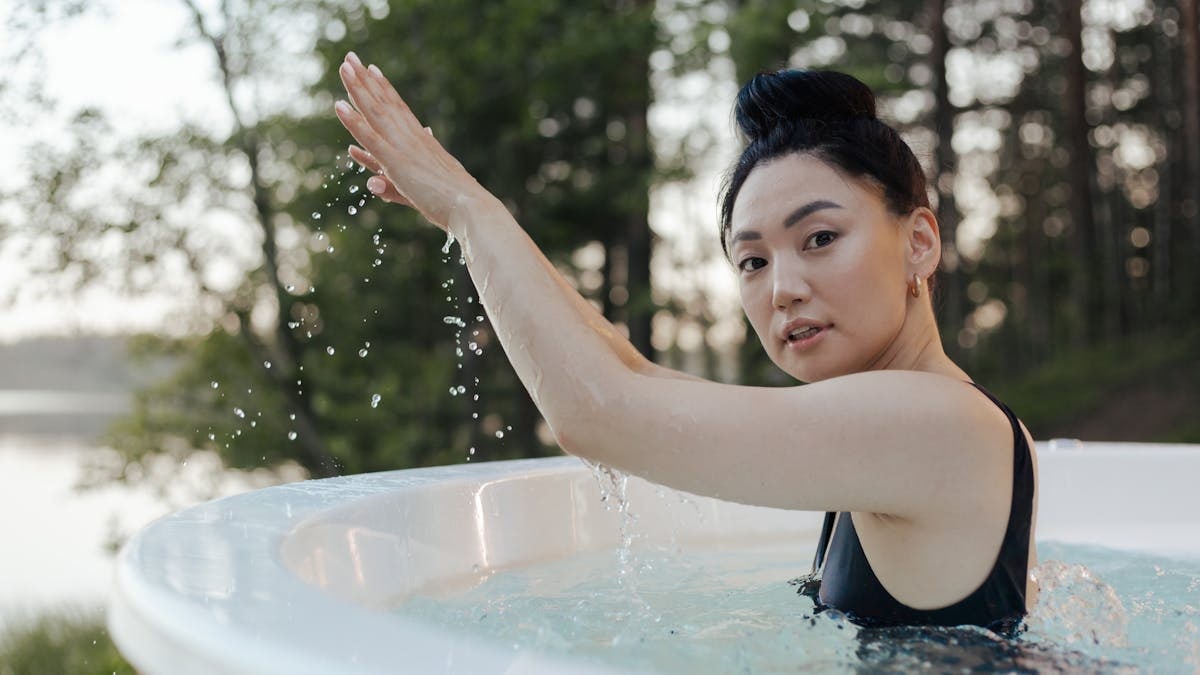An Asian woman enjoys relaxation in an outdoor hot tub surrounded by nature.